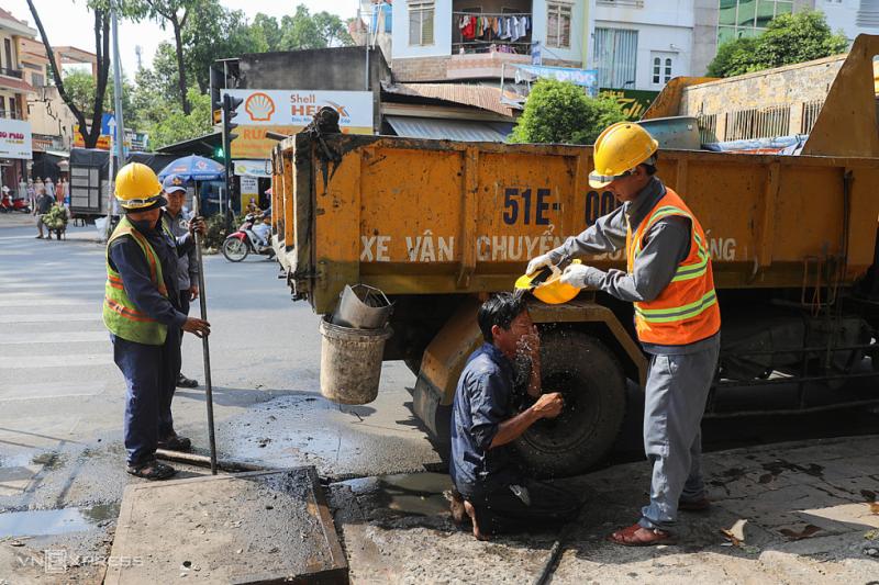 Nhóm công nhân thoát nước đô thị thay phiên nhau xối nước cho mát, tránh sốc nhiệt sau khi móc ống cống ngầm ở TP HCM trong những ngày nắng nóng cực điểm năm 2021. Ảnh: Quỳnh Trần
