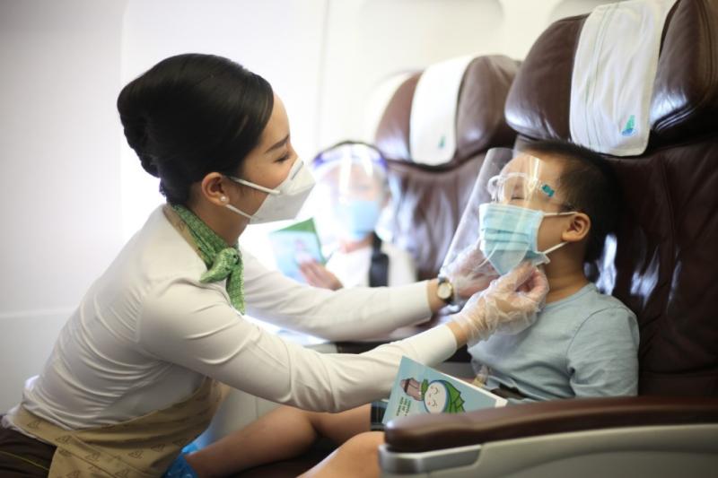 Tiếp viên hàng không Bamboo Airways hỗ trợ khách đeo khẩu trang phòng chống Covid-19 trong một chuyến bay năm 2021. Ảnh: Bamboo Airways